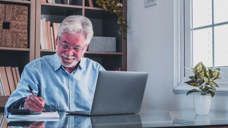 Homme âgé, prenant des notes en écoutant une conférence en ligne