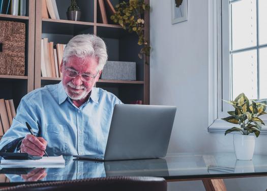 Homme âgé, prenant des notes en écoutant une conférence en ligne